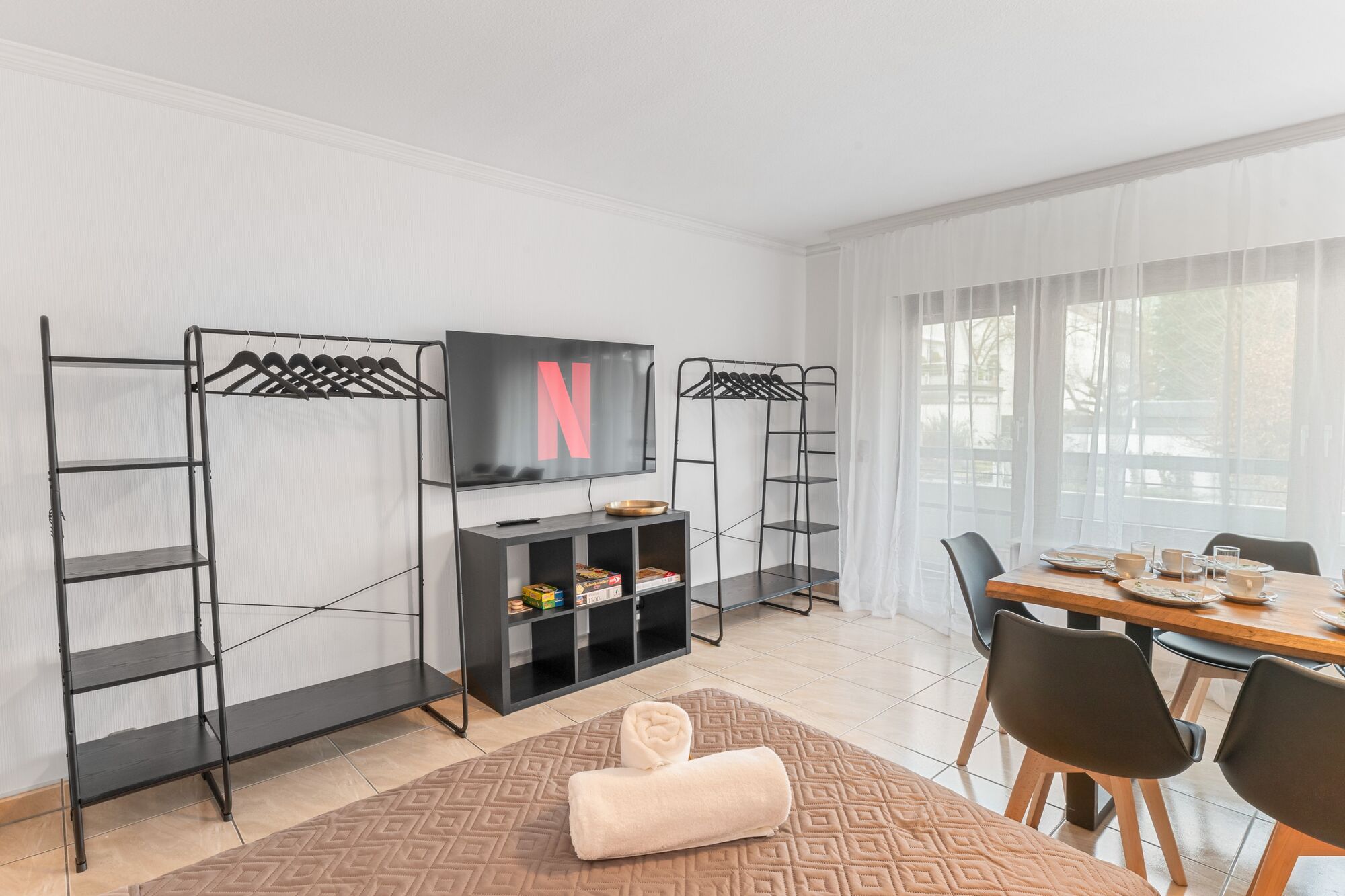 Helles Wohn- und Esszimmer mit 55 Zoll Smart-TV. Offene Kleiderständer und Regale bieten ausreichend Stauraum für längere Aufenthalte. Viel Tageslicht durch große Fensterfront. Helles Wohn- und Esszimmer mit 55 Zoll Smart-TV. Offene Kleiderständer und Regale bieten ausreichend Stauraum für längere Aufenthalte. Viel Tageslicht durch große Fensterfront.