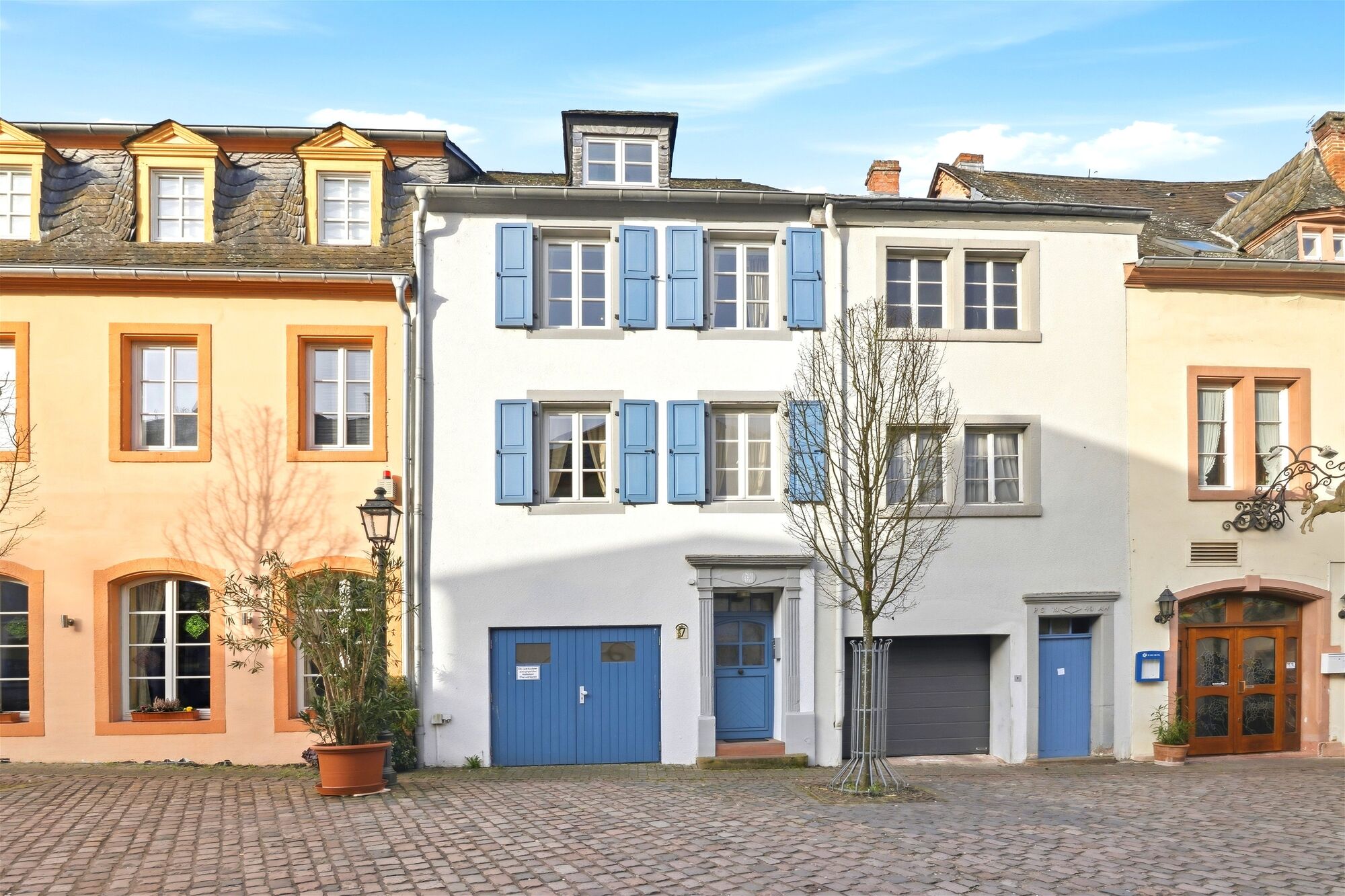 Historisches dreistöckiges Stadthaus mit blauen Fensterläden und blauer Garagentür auf gepflastertem
