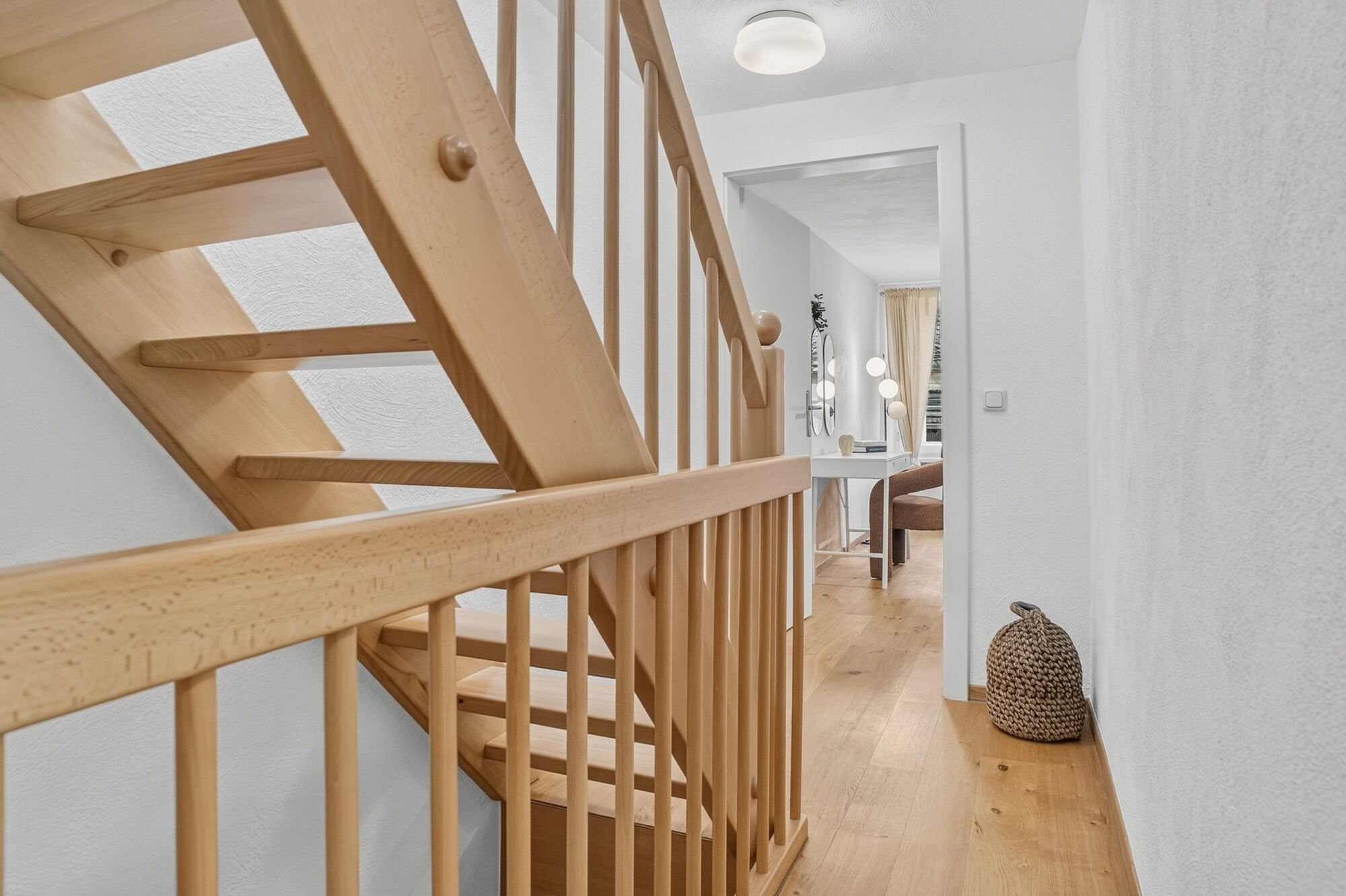 Helles Treppenhaus mit hellem Holzgeländer, Blick auf Flur und Schlafzimmer im Hintergrund.