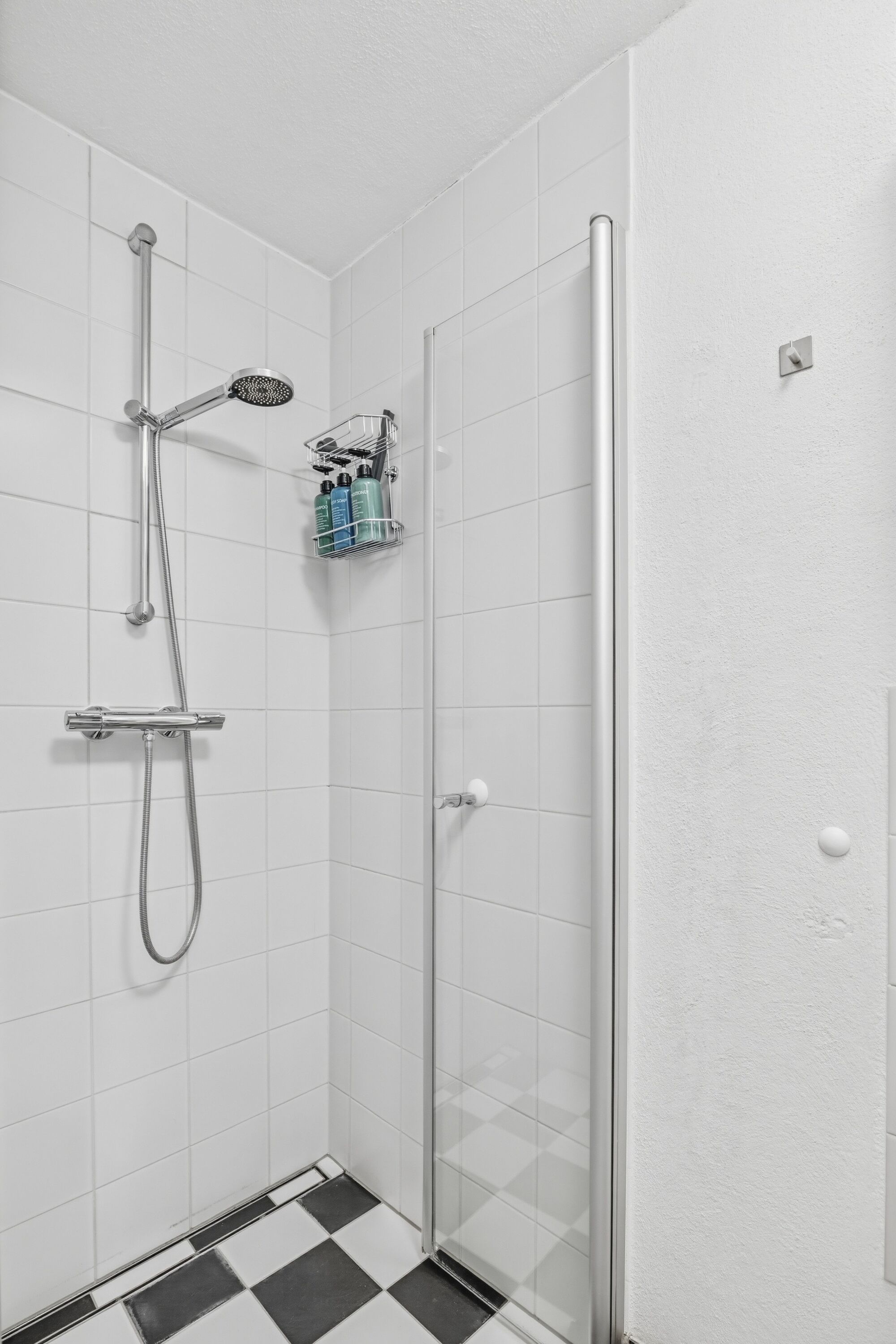 Bodenebene Dusche mit Regenduschkopf, weiße Fliesen, Duschgel-Flaschen an der Wand.