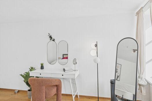 Weißer Schminktisch mit zwei ovalen Spiegeln, terrakottafarbener Sessel, großer Standspiegel, Zimmerpflanze.