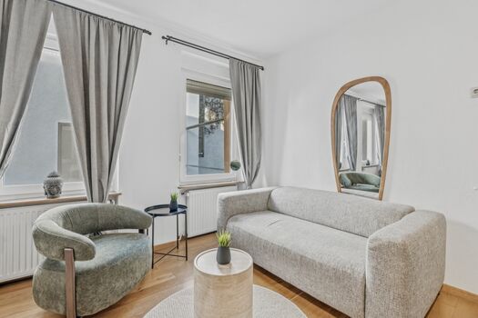 Helles Wohnzimmer mit grauem Sofa, rundem Beistelltisch und großem Spiegel an der Wand.