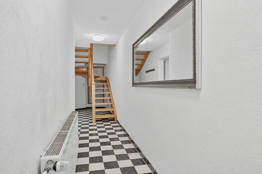 Flur mit schwarz-weißem Schachbrettmuster, Holztreppe, großer Wandspiegel, hohe Decken.