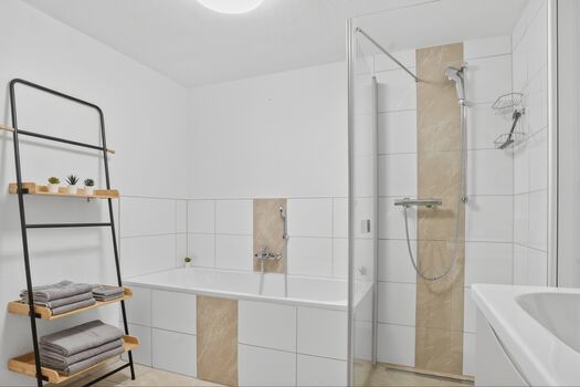 Weißes Badezimmer mit Duschkabine, Badewanne, Handtücher hängen an der Wand.