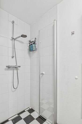 Bodenebene Dusche mit Regenduschkopf, weiße Fliesen, Duschgel-Flaschen an der Wand.