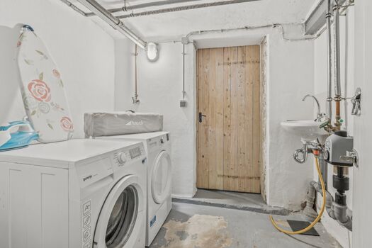 Weiße Einbauwaschmaschine in einem schlichten Hauswirtschaftsraum mit Holztür.