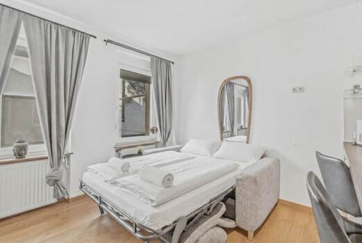 Helles Zimmer mit ausgeklapptem Schlafsofa, pinker Bettwäsche und grauem Vorhang.