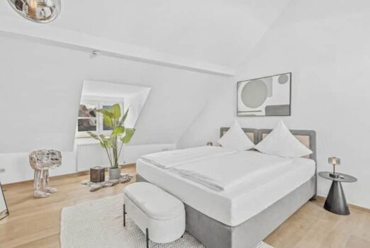 Weißes Doppelzimmer mit grauem Bettrahmen, pinker Bettwäsche und großer Zimmerpflanze.