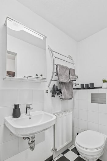 Weißes Badezimmer mit Waschtisch, Spiegel mit Beleuchtung und gefalteten Handtüchern.