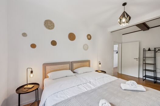 Schlafzimmer 1 mit hochwertigen Boxspringbetten, Nachttischen und einem offenen Kleiderschrank. Die Betten können wahlweise einzeln oder als komfortables Doppelbett gestellt werden.