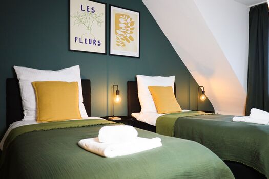 Schlafzimmer 1 - Twin-Schlafzimmer mit zwei Einzelbetten, hochwertiger Bettwäsche, TV, Nachttischlampen und ruhigen Grüntönen. Stilvolle Wandbilder und Nachttischlampen schaffen eine entspannte Atmosphäre für Business-Reisende, Freunde oder Familien mit Fokus auf Komfort: