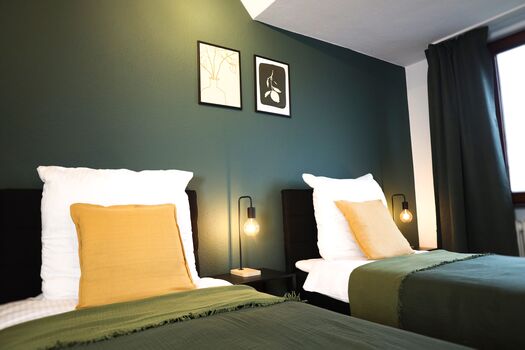 Schlafzimmer 2 - Twin-Schlafzimmer mit zwei Einzelbetten, hochwertiger Bettwäsche, TV, Nachttischlampen und ruhigen Grüntönen.
