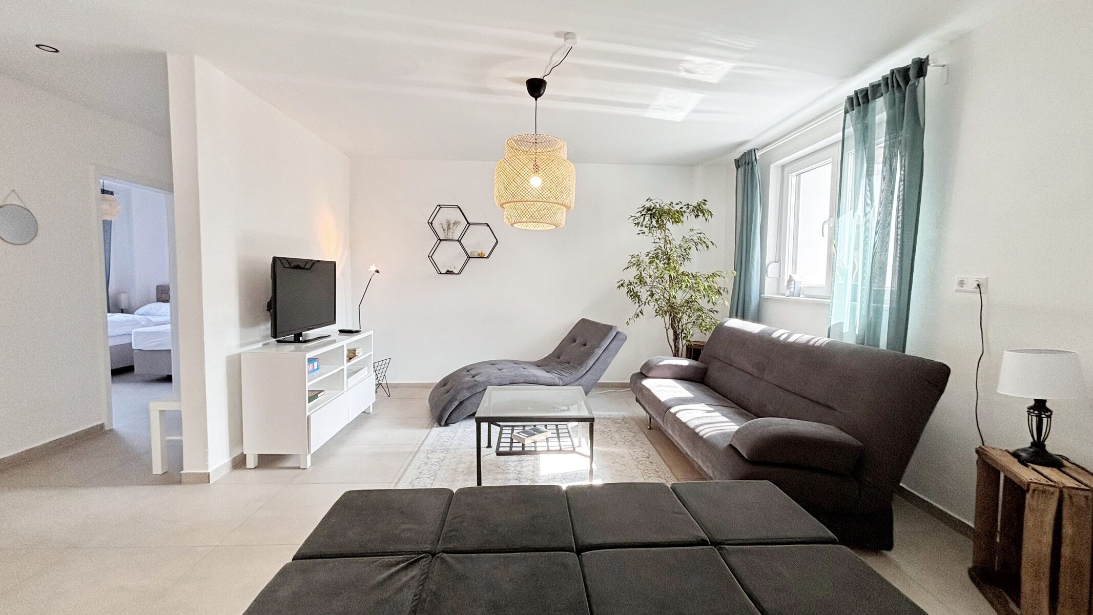 Modernes Wohnzimmer mit gemütlicher Sitzecke, Flachbild-TV, stilvoller Beleuchtung, hellen Fliesen, großen Fenstern und geschmackvoller Deko.