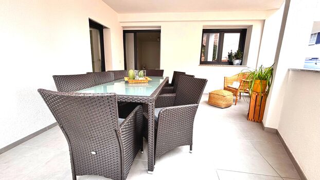 Großer, überdachter Balkon mit gemütlicher Sitzecke und Esstisch für bis zu acht Personen. Ideal zum Entspannen oder für gesellige Abende im Freien – stilvoll möbliert und dekoriert mit Pflanzen und Naturmaterialien.