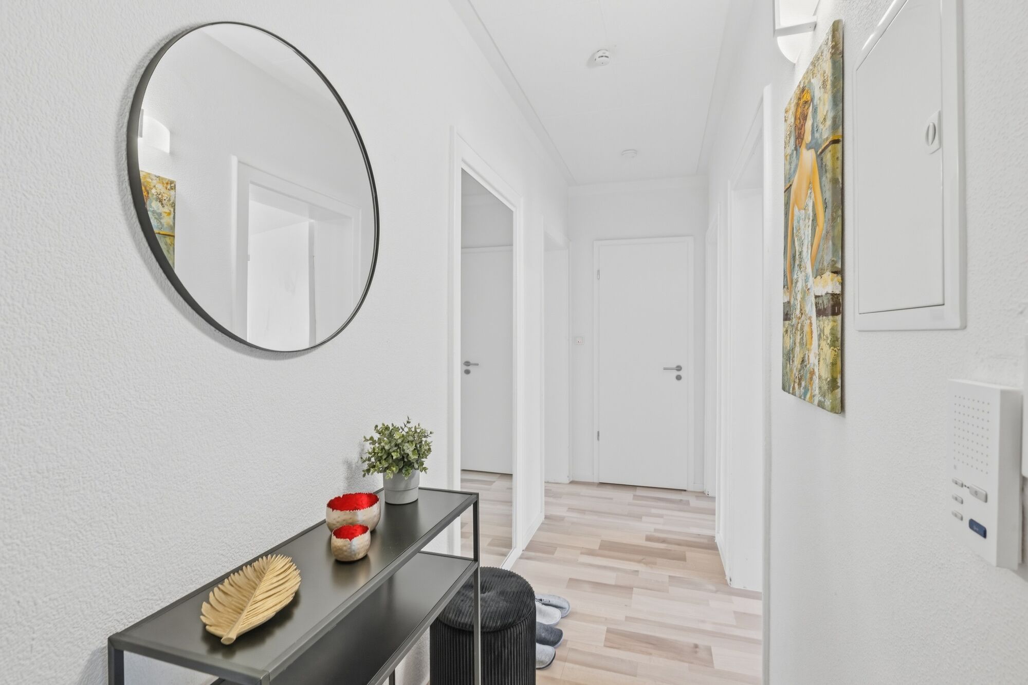 Weißes Bad mit rundem Wandspiegel, schwarzem Waschtisch, Kunstwerk an der Wand, heller Holzboden.