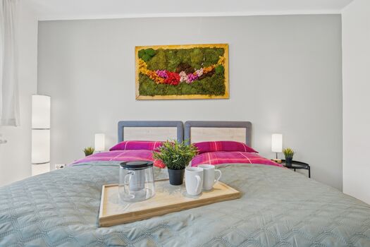 Doppelbett mit pinker Bettwäsche, buntes Moosgemälde an der Wand, Frühstückstablett auf dem Bett.