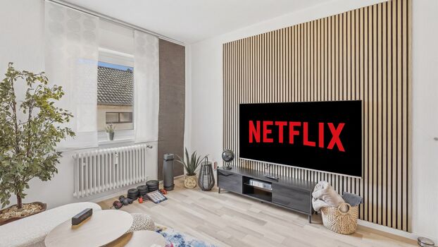 Helles Wohnzimmer mit großem Flachbildschirm, Netflix-Logo, Holzlamellenverkleidung und Zimmerpflanz