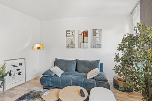 Blaues Sofa mit Kissen, runde Beistelltische, goldene Wandleuchte, heller Holzboden.